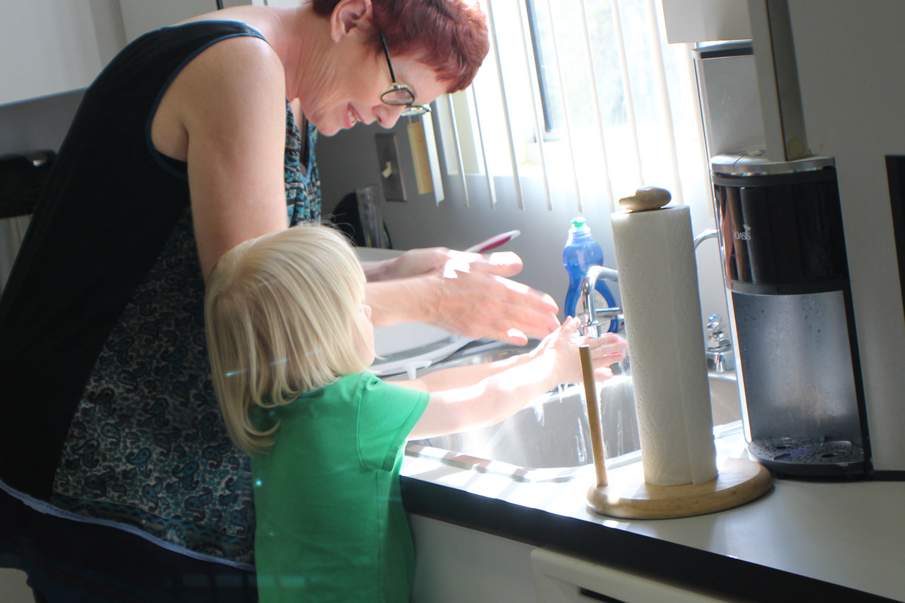 an image of a volunteer helping to teach a school age child how to navigate and find objects around a kitchen sink