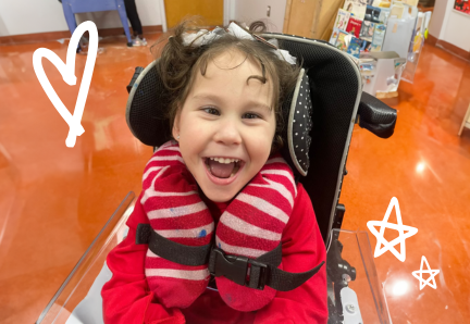 5oo A young child in a wheelchair laughs joyfully indoors, wearing a striped neck pillow.