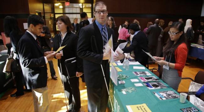 A few people who are blind or visually impaired at a career fair gathered in front of an employer's table listening to the employer talk