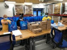Image of three Lighthouse Works fulfillment specialists wearing facemasks and assembling care packages.