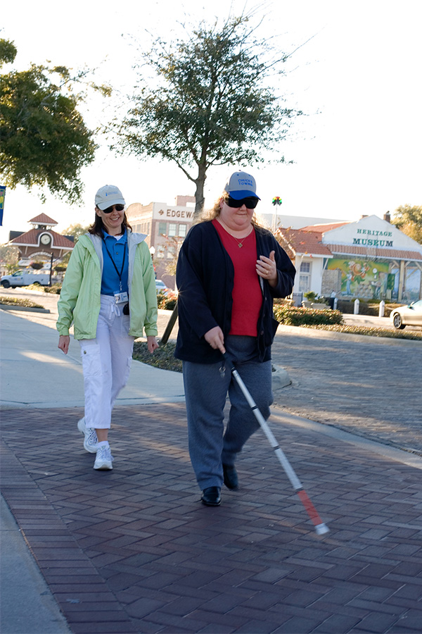 Image of a woman who is blind crossing the street with a white cane